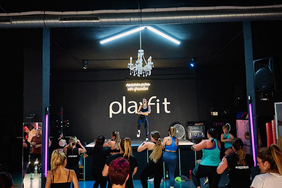 Entrenadora sobre la tarima dando clase y las alumnas abajo siguiéndola, en la sala fitness Playfit Boutique Algeciras.